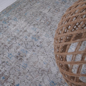 May include: A light blue and brown patterned rug with a woven, light brown, round lampshade on top of it.
