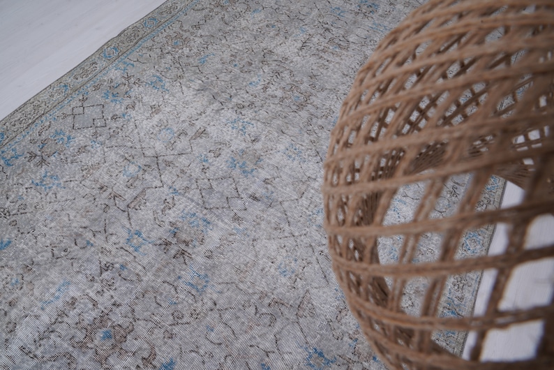May include: A light blue and brown patterned rug with a woven, light brown, round lampshade on top of it.