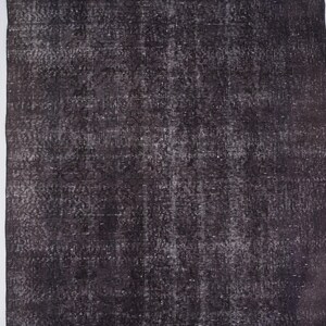Puede incluir: Una alfombra rectangular de color marr&oacute;n oscuro con un aspecto envejecido. La alfombra tiene un patr&oacute;n descolorido y moteado con acentos m&aacute;s claros. La alfombra est&aacute; colocada junto a un suelo de madera blanco.