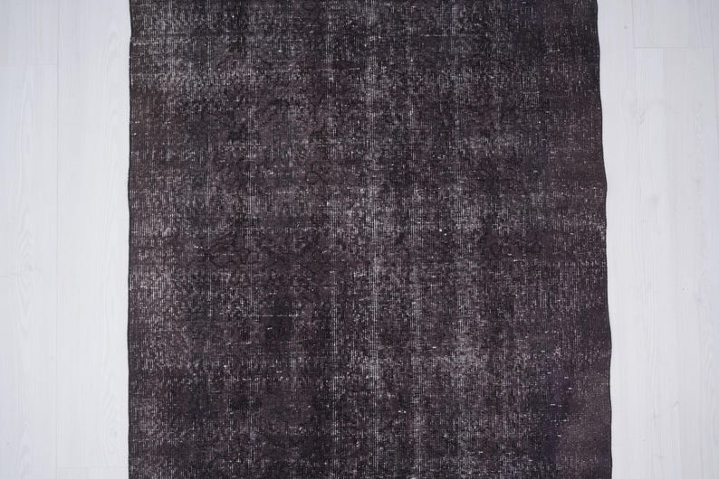 Puede incluir: Una alfombra rectangular de color marr&oacute;n oscuro con un aspecto envejecido. La alfombra tiene un patr&oacute;n descolorido y moteado con acentos m&aacute;s claros. La alfombra est&aacute; colocada junto a un suelo de madera blanco.