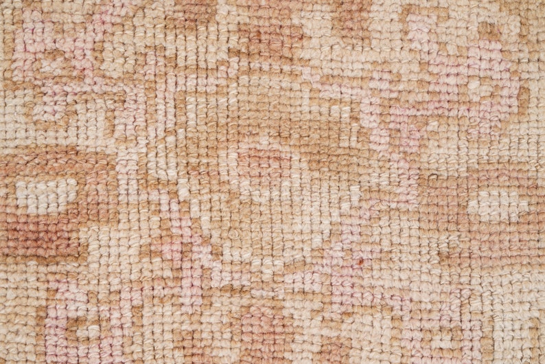 May include: Close-up of a beige and pink woven rug with a textured surface. The rug has a subtle pattern of small, repeating shapes.