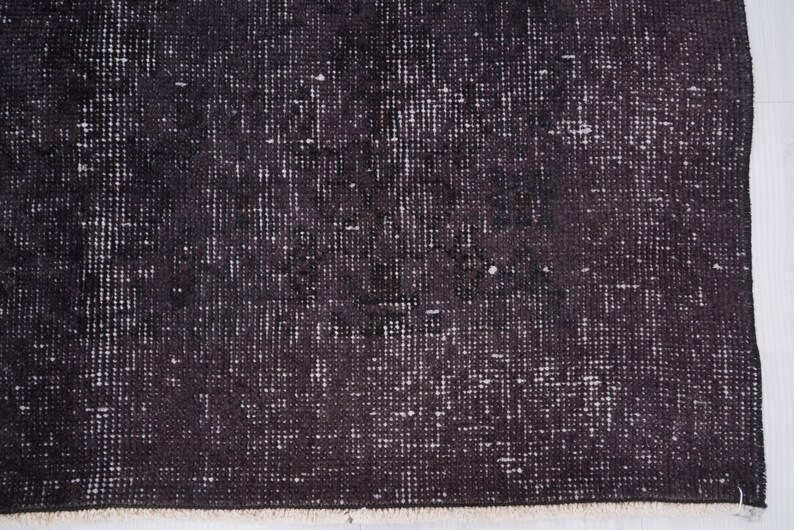 Puede incluir: Primer plano de una alfombra oscura y texturizada con aspecto envejecido. La alfombra tiene una combinaci&oacute;n de colores blanco y negro, con un patr&oacute;n de peque&ntilde;os puntos y l&iacute;neas blancas irregulares sobre un fondo oscuro. Los bordes de la alfombra est&aacute;n deshilachados.