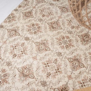 Peut inclure: Un tapis vintage de couleur cr&egrave;me avec un motif floral d&eacute;licat dans des tons de brun et de rose.