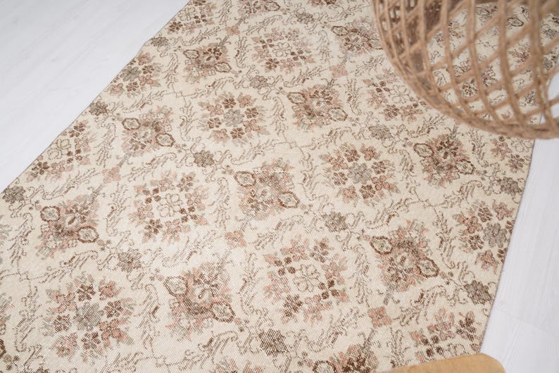 Peut inclure: Un tapis vintage de couleur cr&egrave;me avec un motif floral d&eacute;licat dans des tons de brun et de rose.