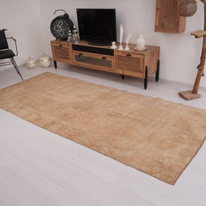May include: A light brown area rug with a subtle pattern. The rug is laid out on a white wood floor in a living room setting.