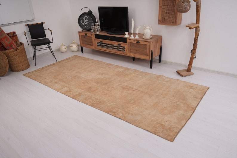 May include: A light brown area rug with a subtle pattern. The rug is laid out on a white wood floor in a living room setting.