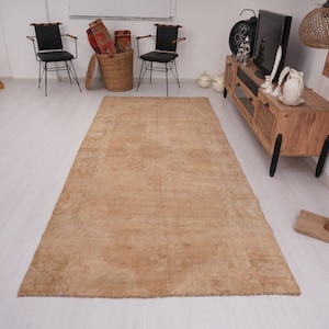 May include: A light brown area rug with a subtle pattern. The rug is laid out on a white floor in a room with furniture.