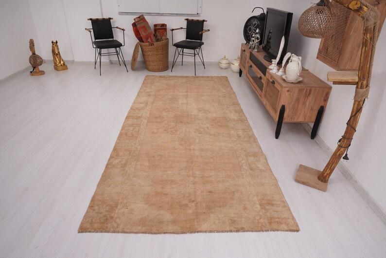 May include: A light brown area rug with a subtle pattern. The rug is laid out on a white floor in a room with furniture.