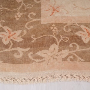 May include: A beige rug with a floral pattern in shades of brown and orange. The rug has a fringe border.