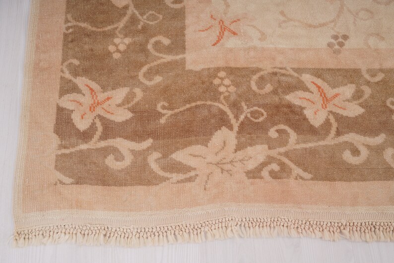 May include: A beige rug with a floral pattern in shades of brown and orange. The rug has a fringe border.