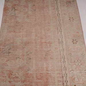 May include: A vintage runner rug with a faded pink and cream color scheme. The rug has a distressed look with a subtle pattern throughout.