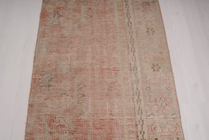 May include: A vintage runner rug with a faded pink and cream color scheme. The rug has a distressed look with a subtle pattern throughout.