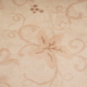 May include: A close-up of a beige rug with a floral pattern. The pattern is made up of brown and beige swirls and leaves.