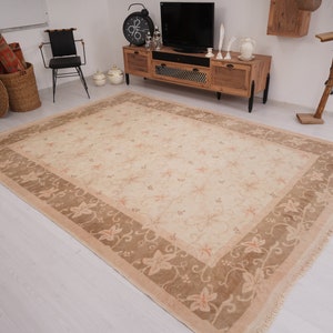 May include: A beige area rug with a floral pattern in a light brown color. The rug has a fringe border.