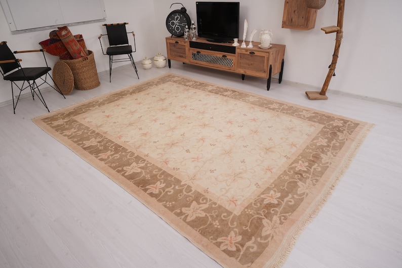May include: A beige area rug with a floral pattern in a light brown color. The rug has a fringe border.