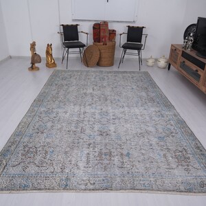 May include: A light blue and gray vintage rug with a faded floral pattern. The rug is laid out on a light wood floor in a living room setting.