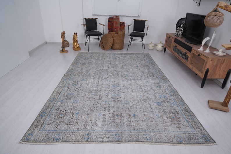 May include: A light blue and gray vintage rug with a faded floral pattern. The rug is laid out on a light wood floor in a living room setting.