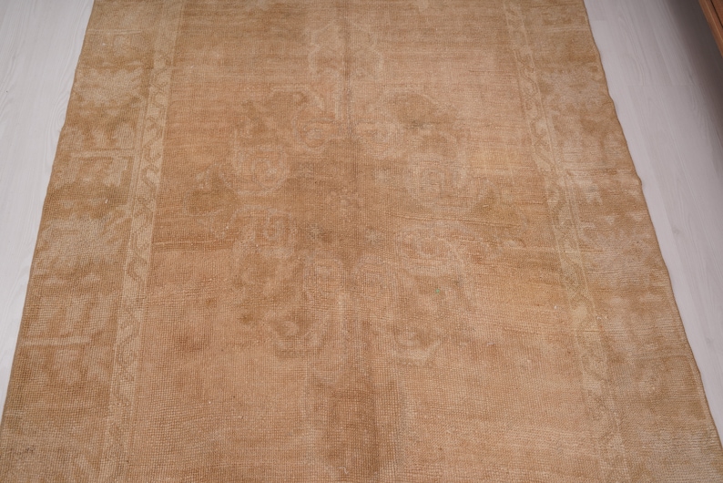 May include: A light brown rug with a subtle pattern. The rug has a worn, vintage look and is made of a soft, natural material.