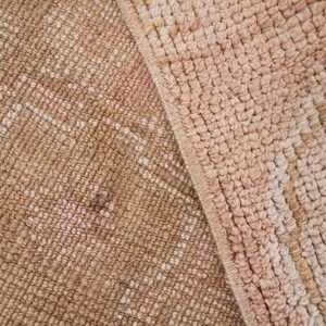May include: Close-up of a woven rug with a pink and brown color scheme. The rug has a textured surface and a subtle pattern.