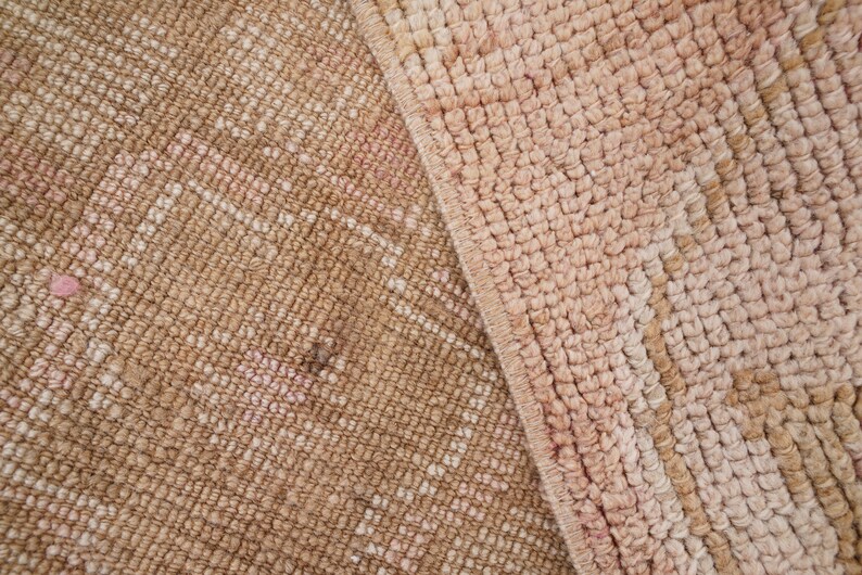 May include: Close-up of a woven rug with a pink and brown color scheme. The rug has a textured surface and a subtle pattern.