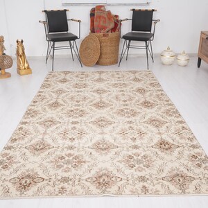 Peut inclure: Un tapis de couleur cr&egrave;me avec un motif floral dans des tons de brun. Le tapis est pos&eacute; sur un sol en bois clair dans une pi&egrave;ce aux murs blancs.