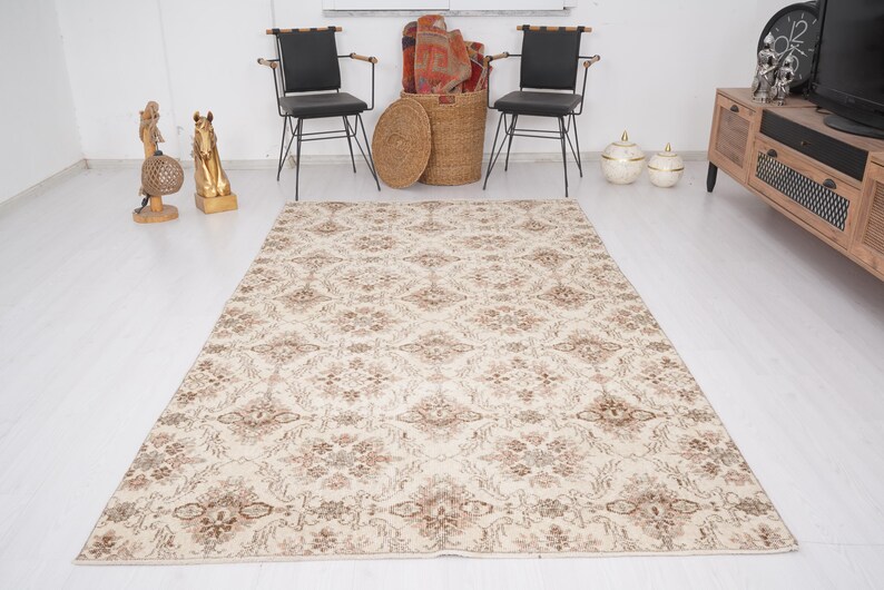Peut inclure: Un tapis de couleur cr&egrave;me avec un motif floral dans des tons de brun. Le tapis est pos&eacute; sur un sol en bois clair dans une pi&egrave;ce aux murs blancs.