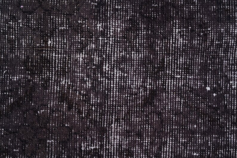 Puede incluir: Primer plano de una alfombra desgastada en blanco y negro. La alfombra tiene un aspecto texturizado con un patr&oacute;n de l&iacute;neas verticales y motas blancas dispersas. El color oscuro le da un aspecto vintage o antiguo.