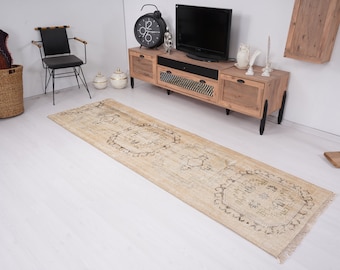 Op de afbeelding: Een beige loper met een traditioneel patroon in lichtbruin. De loper ligt op een witte houten vloer in een woonkamer.