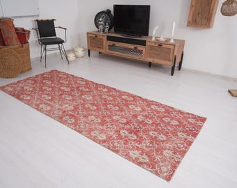May include: A rectangular, distressed red rug with a floral pattern. The rug is laid out on a white floor, and the design features cream-colored floral motifs. The rug is a long, narrow runner, suitable for hallways or entryways.