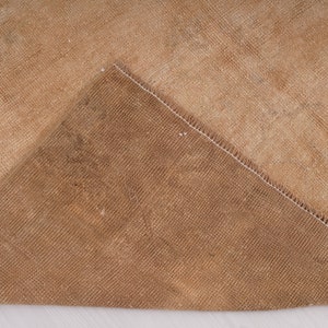 May include: Close-up of the back side of a tan rug with a white seam. The rug has a woven texture.