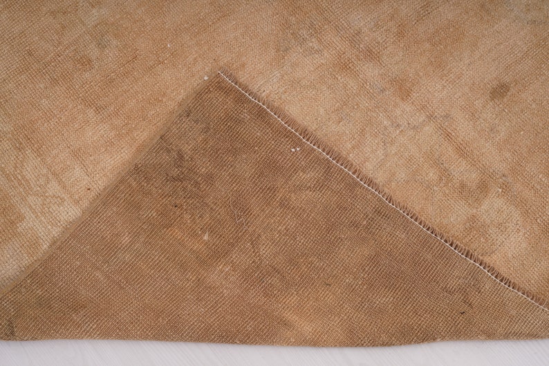 May include: Close-up of the back side of a tan rug with a white seam. The rug has a woven texture.