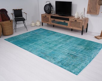 May include: A teal blue vintage rug with a distressed look. The rug is laid out on a white floor in a room with furniture.