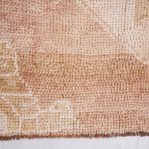 May include: A close-up of a beige and brown woven rug with a geometric pattern. The rug has a fringe border.