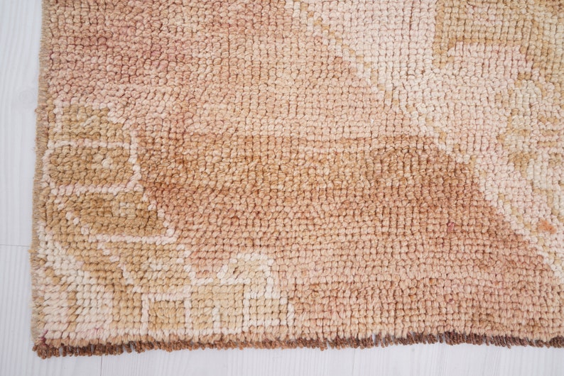 May include: A close-up of a beige and brown woven rug with a geometric pattern. The rug has a fringe border.