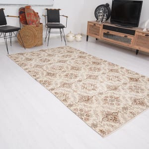 Peut inclure: Un tapis de couleur cr&egrave;me avec un motif floral brun. Le tapis est pos&eacute; sur un sol en bois blanc dans un salon.