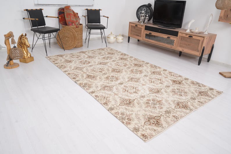 Peut inclure: Un tapis de couleur cr&egrave;me avec un motif floral brun. Le tapis est pos&eacute; sur un sol en bois blanc dans un salon.