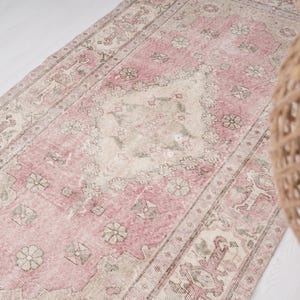 Puede incluir: Alfombra rectangular de aspecto envejecido, con una paleta de colores rosa y beige descoloridos. La alfombra presenta un diseño central de medallón y patrones florales. Mide aproximadamente 90 x 180 cm.