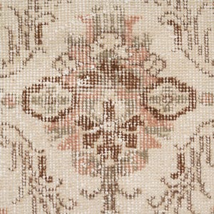 Peut inclure: Gros plan d'un tapis beige avec un motif floral dans les tons de brun, rose et vert. Le tapis a une texture tiss&eacute;e et un design d&eacute;licat.