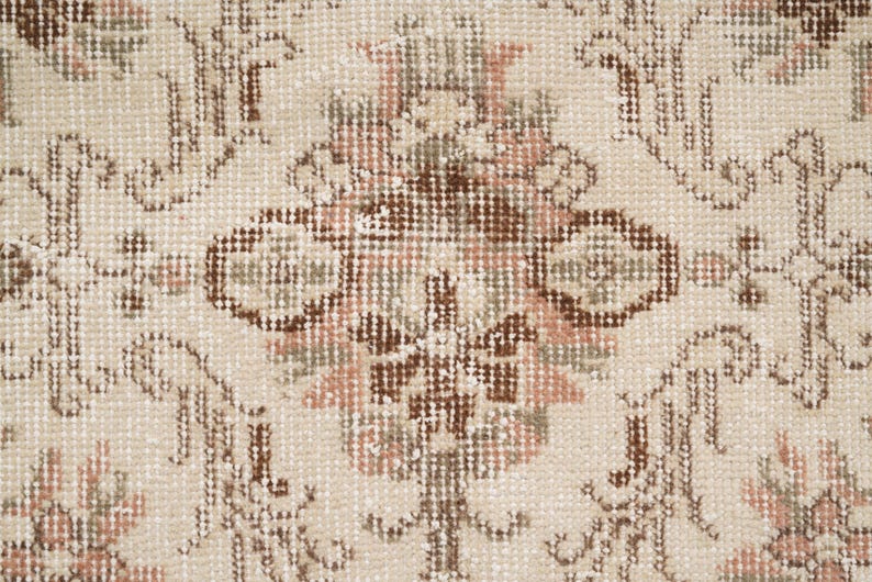Peut inclure: Gros plan d'un tapis beige avec un motif floral dans les tons de brun, rose et vert. Le tapis a une texture tiss&eacute;e et un design d&eacute;licat.