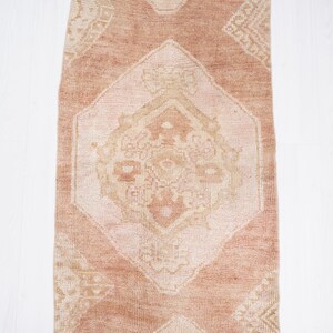 May include: A vintage runner rug with a light pink background and a white geometric pattern. The rug has a distressed look and is perfect for adding a touch of bohemian style to your home.