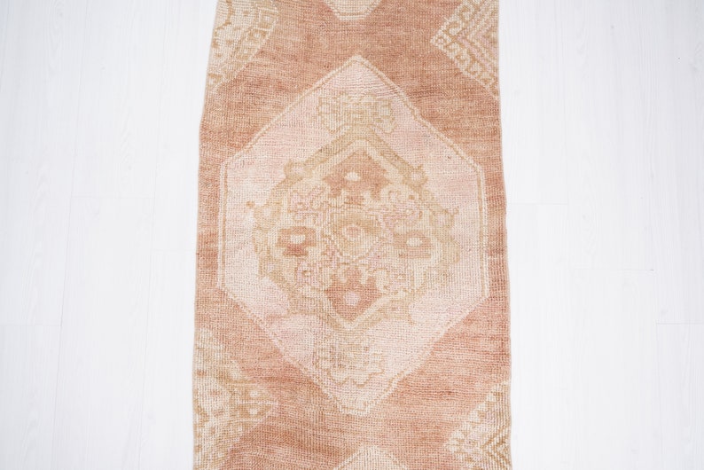 May include: A vintage runner rug with a light pink background and a white geometric pattern. The rug has a distressed look and is perfect for adding a touch of bohemian style to your home.