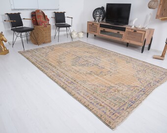 May include: A beige vintage rug with a floral pattern in shades of blue, green, and purple. The rug has a fringed edge and is laid out on a white wooden floor.