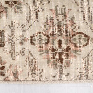Peut inclure: Gros plan sur un tapis beige avec un motif floral brun et rose. Le tapis a une bordure frang&eacute;e.