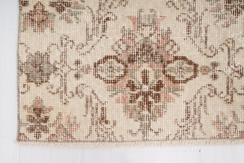 Peut inclure: Gros plan sur un tapis beige avec un motif floral brun et rose. Le tapis a une bordure frang&eacute;e.