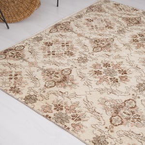 Peut inclure: Un tapis vintage de couleur cr&egrave;me avec un motif floral dans les tons de brun et de rose. Le tapis a un aspect vieilli et est parfait pour ajouter une touche de charme vintage &agrave; n'importe quelle pi&egrave;ce.