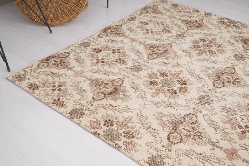 Peut inclure: Un tapis vintage de couleur cr&egrave;me avec un motif floral dans les tons de brun et de rose. Le tapis a un aspect vieilli et est parfait pour ajouter une touche de charme vintage &agrave; n'importe quelle pi&egrave;ce.