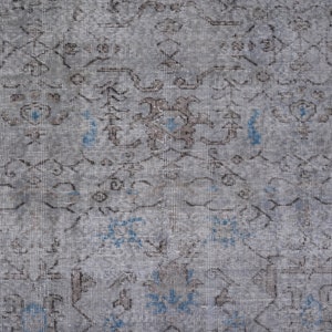 May include: A close-up of a gray and blue patterned rug with a faded, vintage look. The rug has a subtle, intricate design with a repeating pattern of floral motifs.