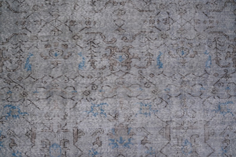 May include: A close-up of a gray and blue patterned rug with a faded, vintage look. The rug has a subtle, intricate design with a repeating pattern of floral motifs.