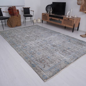 May include: A light blue and gray patterned rug with a faded, vintage look. The rug is laid out on a white wood floor in a living room setting.