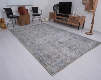 May include: A light blue and gray patterned rug with a faded, vintage look. The rug is laid out on a white wood floor in a living room setting.